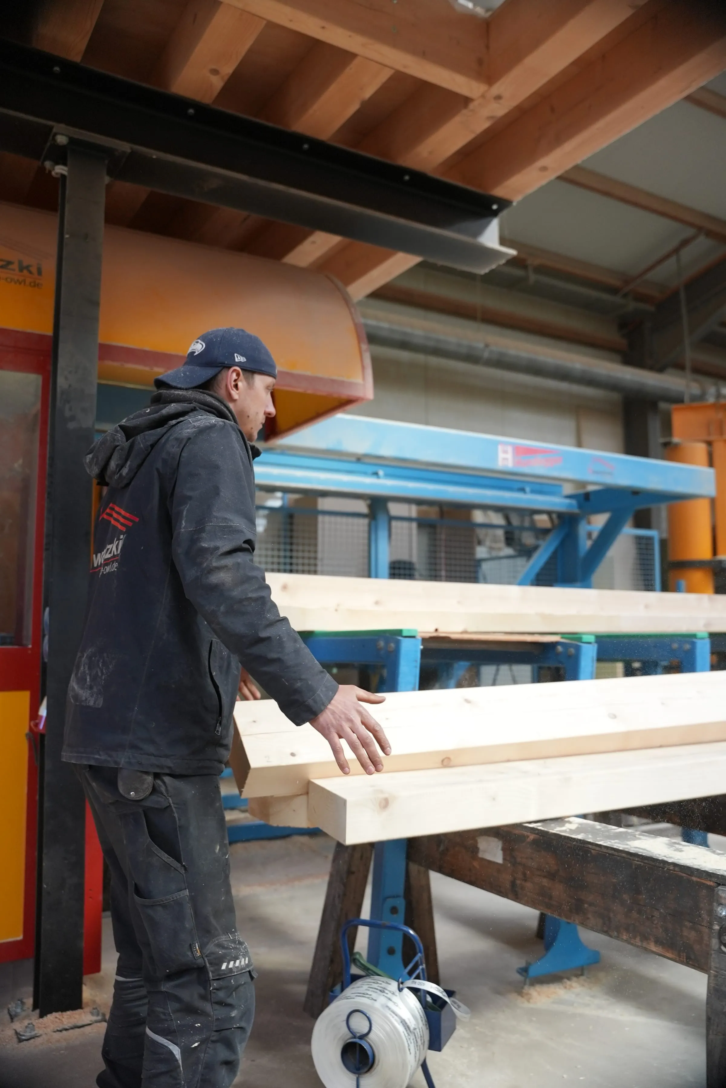 Mitarbeiter führt abgebundene Holzbalken an der Abbundanlage in der Halle