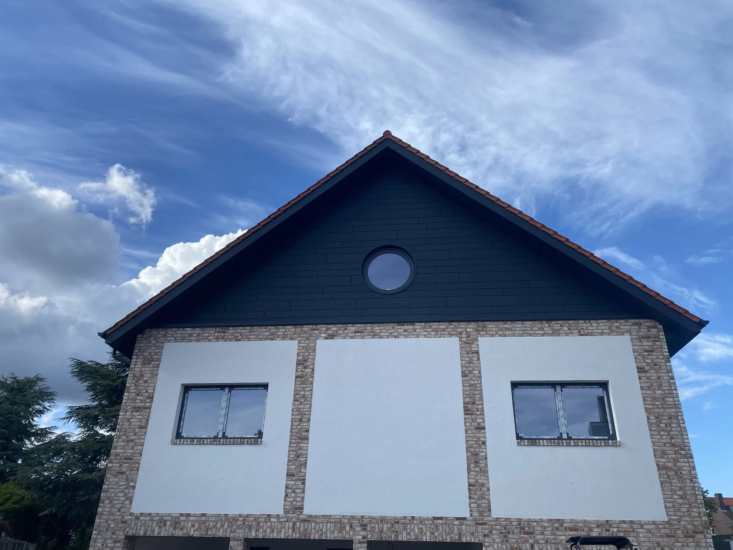 Giebelfläche mit dunkler Blechbekleidung und rundem Fenster
