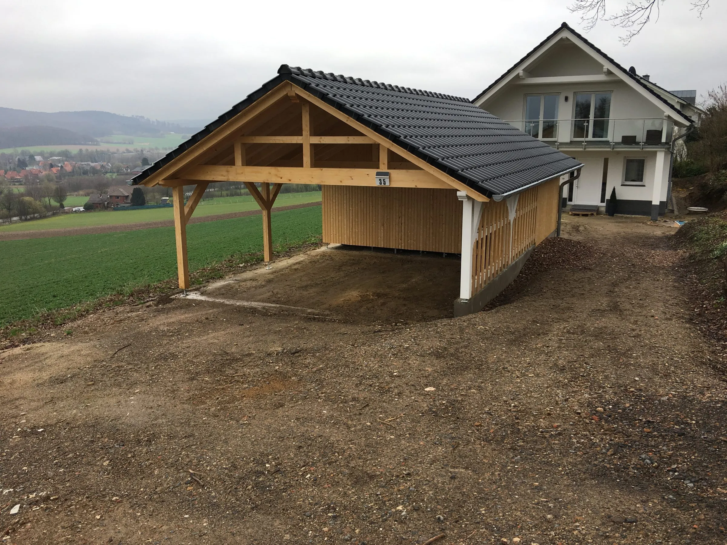 Freistehender Carport aus Holz mit Satteldach und dunkler Eindeckung neben einem Wohnhaus