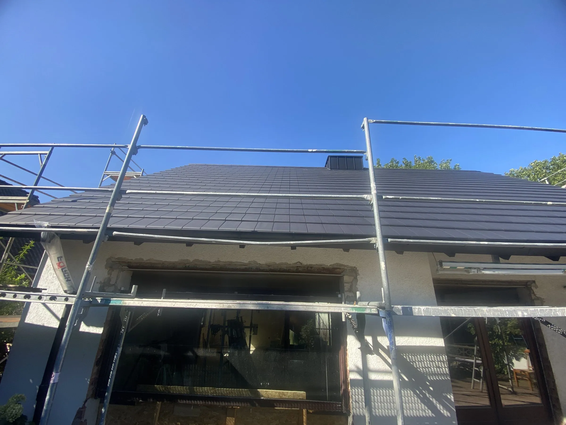 Fertig eingedeckte Dachfläche mit eingebautem Dachflächenfenster an einem eingerüsteten Wohnhaus