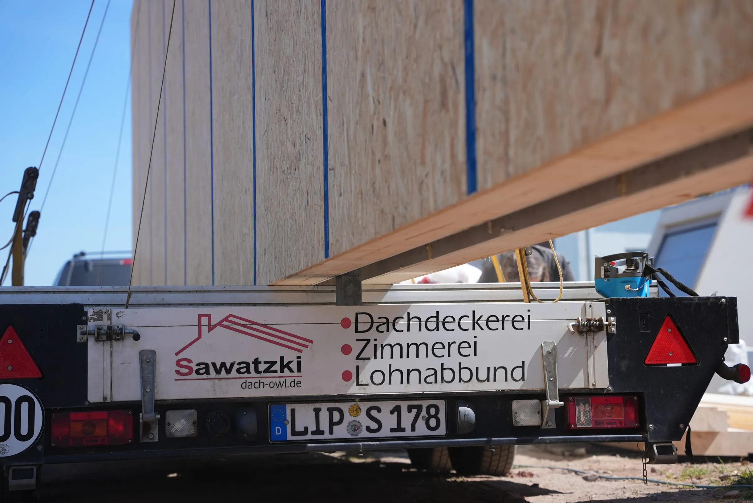 Vorgefertigtes Wandelement auf dem Sawatzki-Anhänger mit der Beschriftung Dachdeckerei, Zimmerei, Lohnabbund