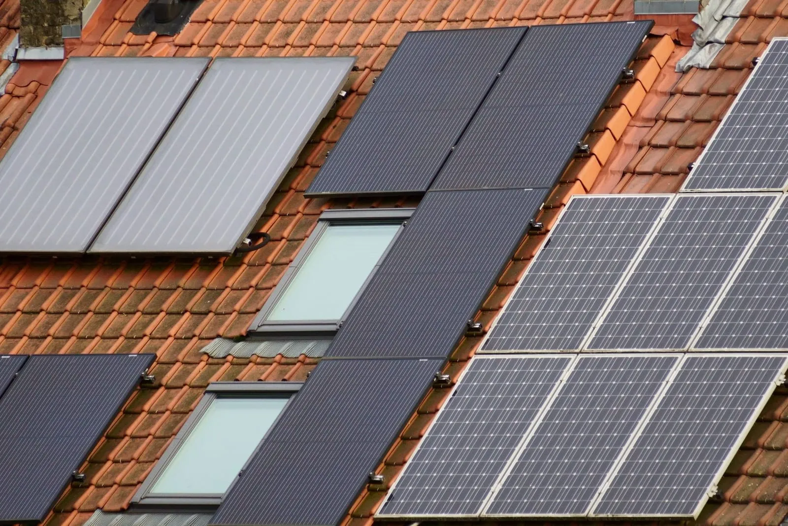 Photovoltaik-Module, Solarthermie-Kollektoren und Dachfenster auf einem roten Ziegeldach (Symbolbild)