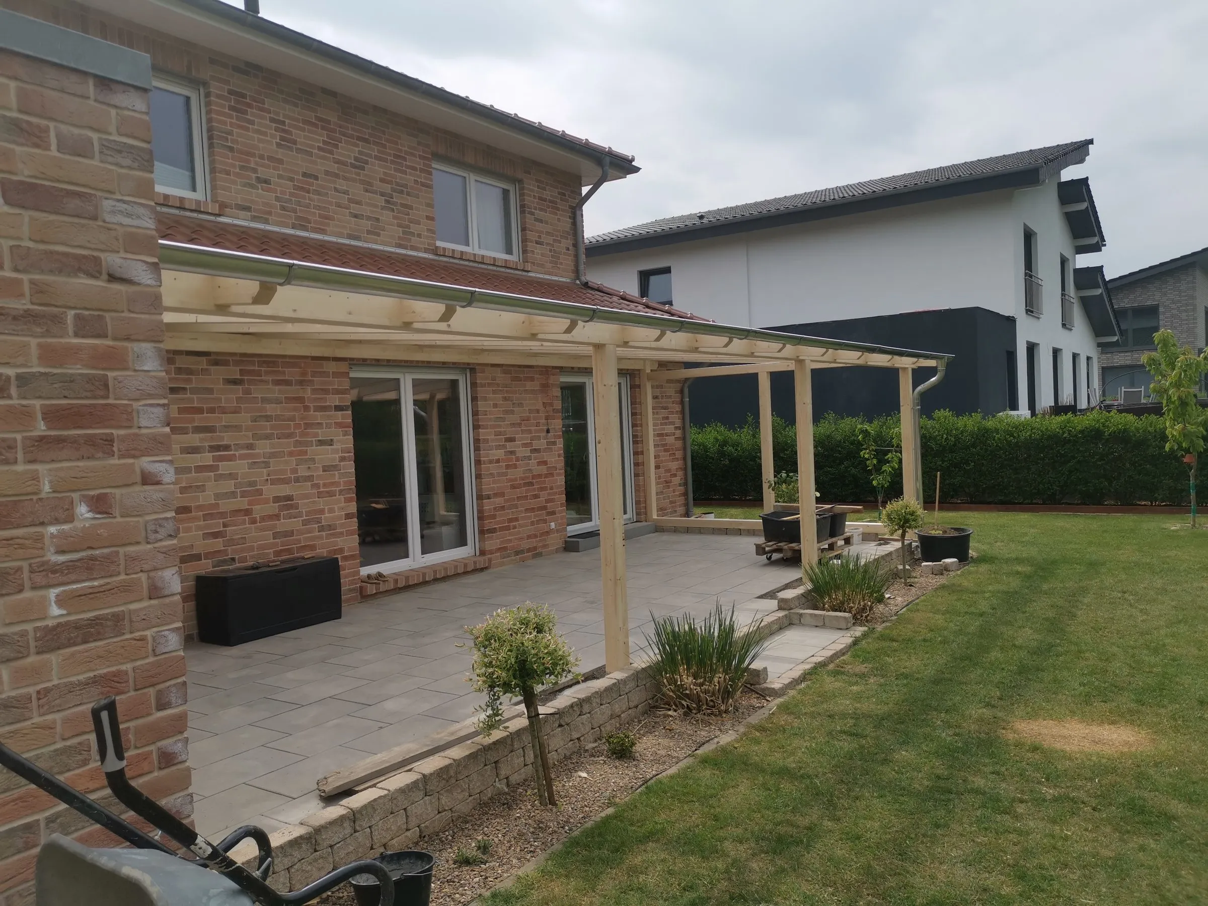 Fertige Terrassenüberdachung aus Holz entlang der Terrasse eines Klinkerhauses